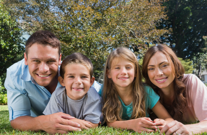 A family of four lying in a garden and smiling towards the camera